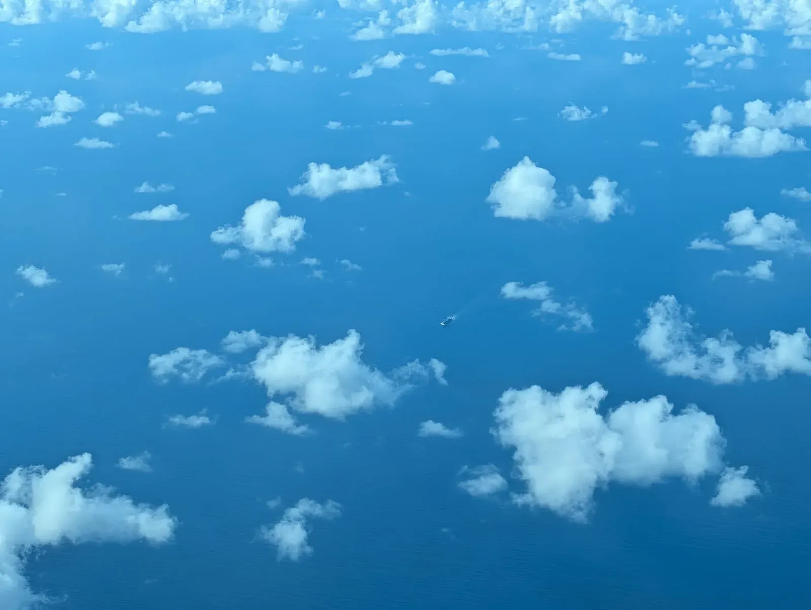 Scattered white clouds over a blue sea, seen from above