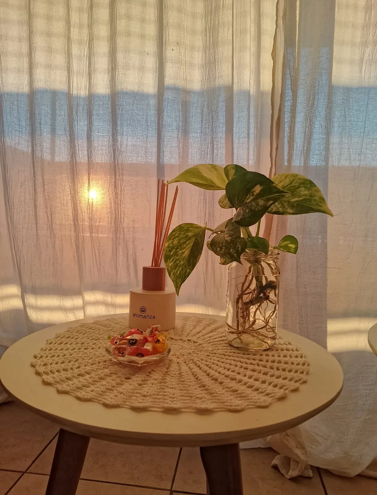 A corner of the consulting room: side table with an aroma diffuser, plants and warm light through sheer curtains