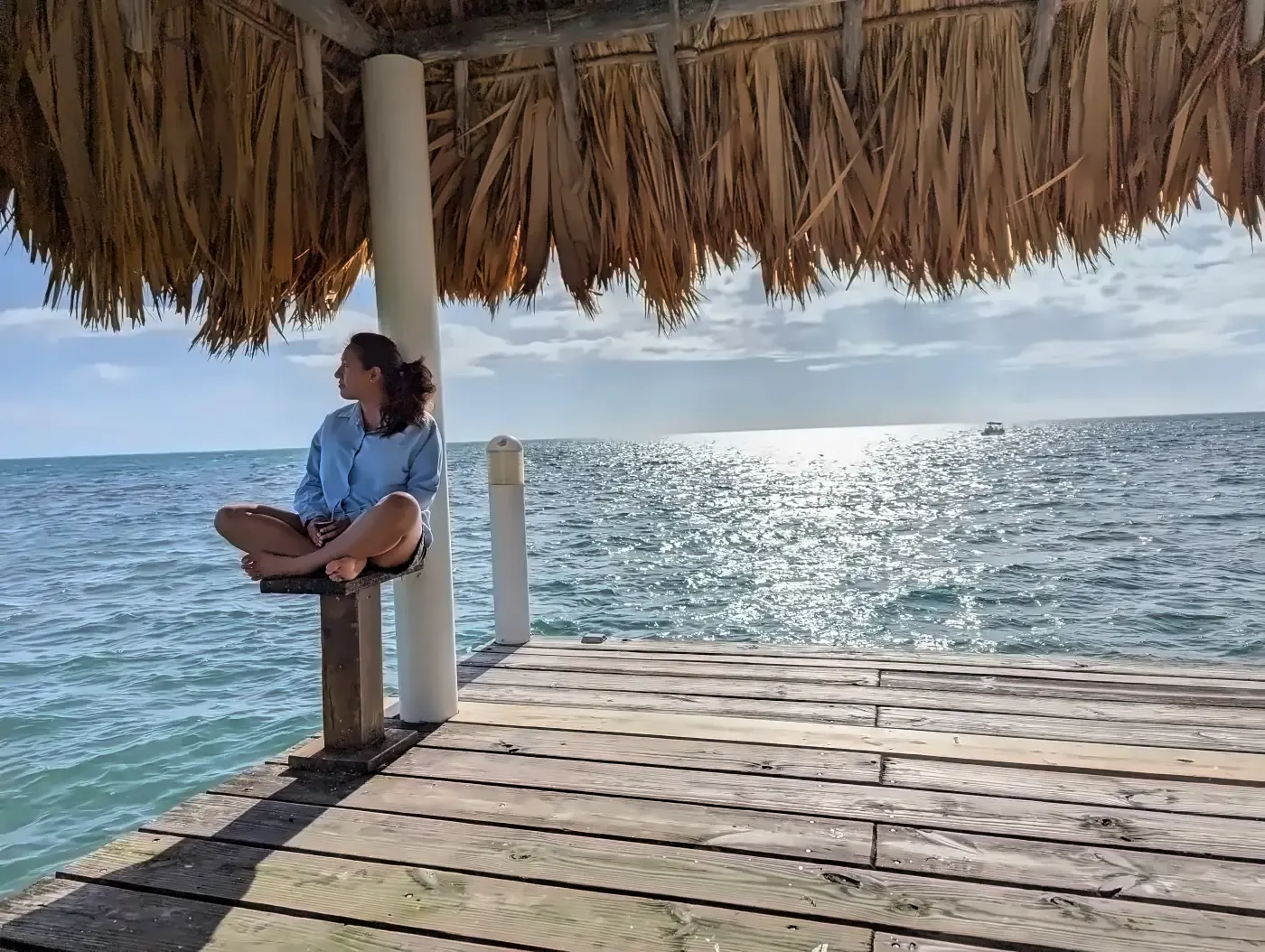 María Eugenia sentada frente al mar, en calma bajo una sombrilla de paja